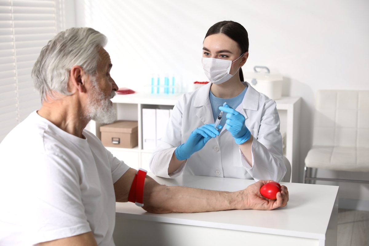 Older man preparing for testosterone blood test results appointment with female medical provider holding syringe in clinical setting