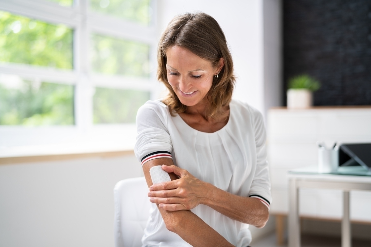 Woman applying HRT delivery methods transdermal patch to her upper arm at home
