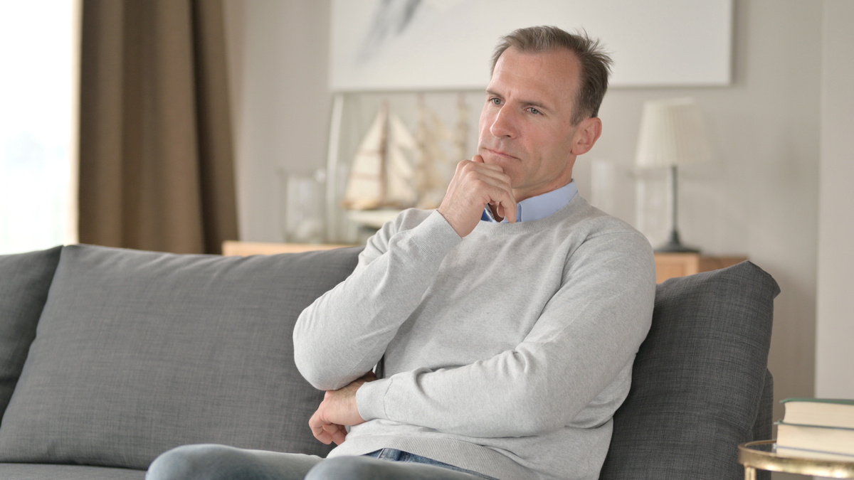 Man in his 40s sitting alone on couch in quiet reflection representing the emotional impact of TRT and depression