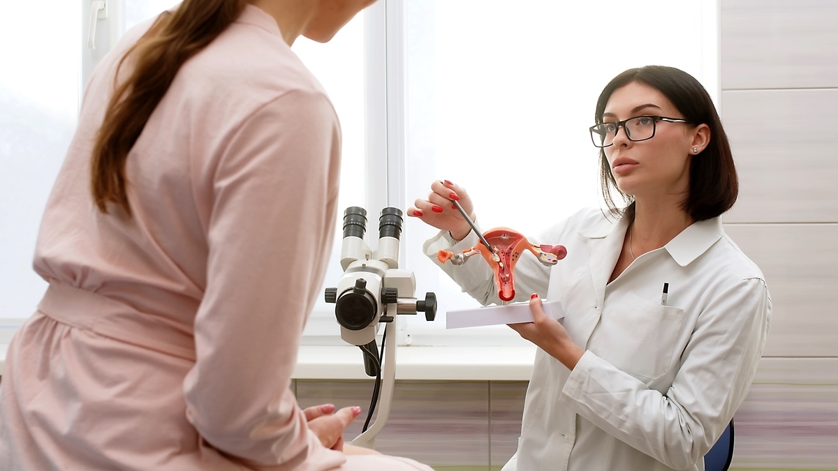 Provider explaining the role of progesterone in HRT to a female patient using a uterine model
