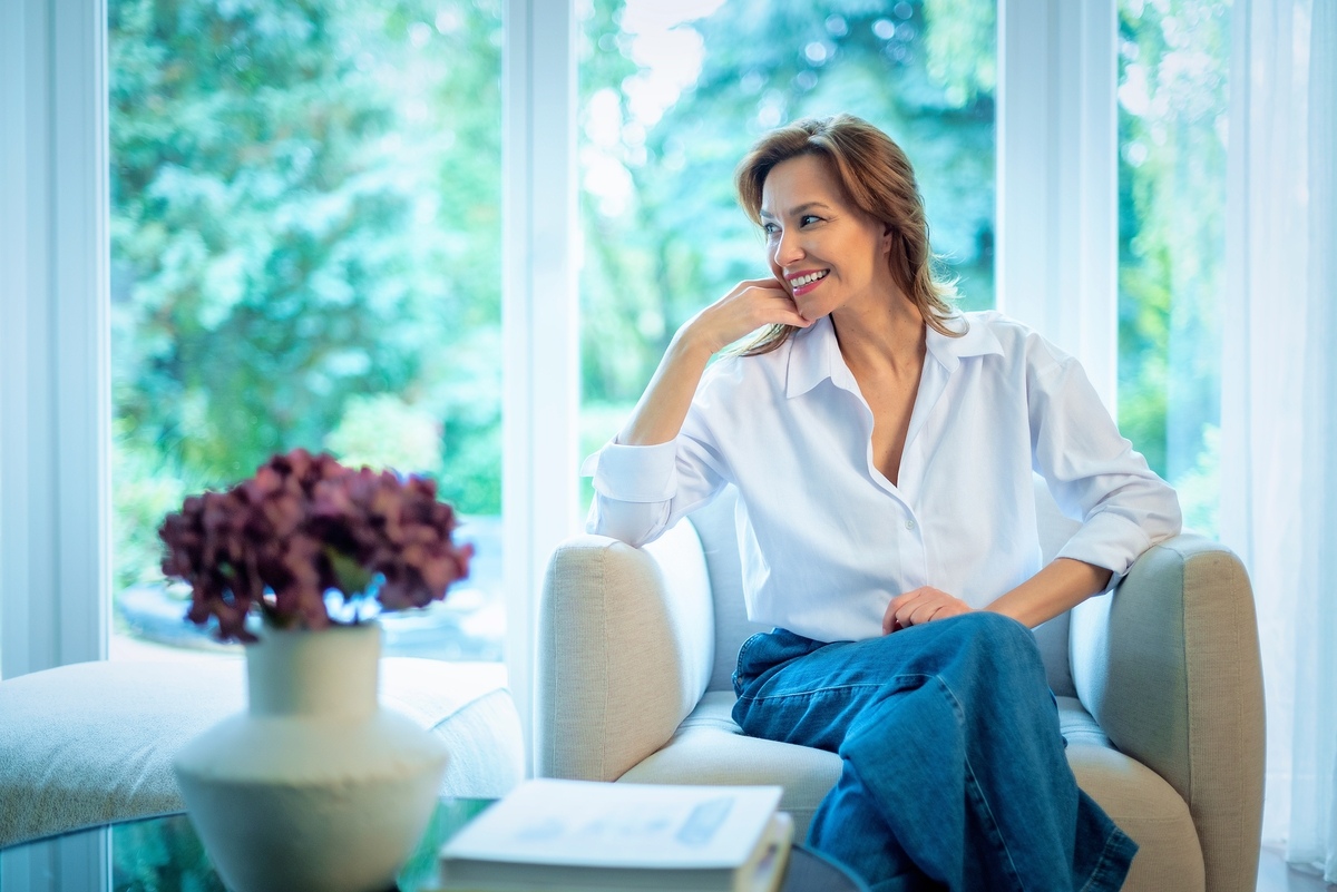 Age to start HRT shown through a smiling woman relaxing confidently at home